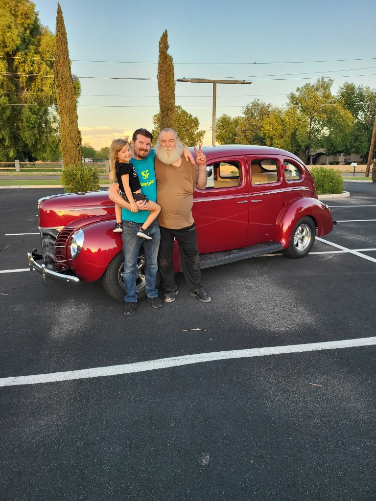 James, Heartley, and Papaw beside the red hot rod — peace sign